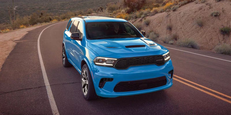A bright blue Dodge Durango driving along a winding mountain road at dusk.